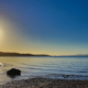 Calm Scottish sea loch viewed from the shore under a bright blue sky, symbolising peace and reflection.