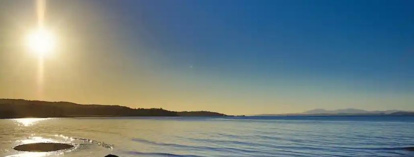 Calm Scottish sea loch viewed from the shore under a bright blue sky, symbolising peace and reflection.